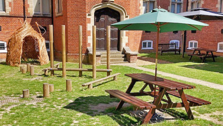 Tring outdoor quad with wooden tables and benches with a green parasol